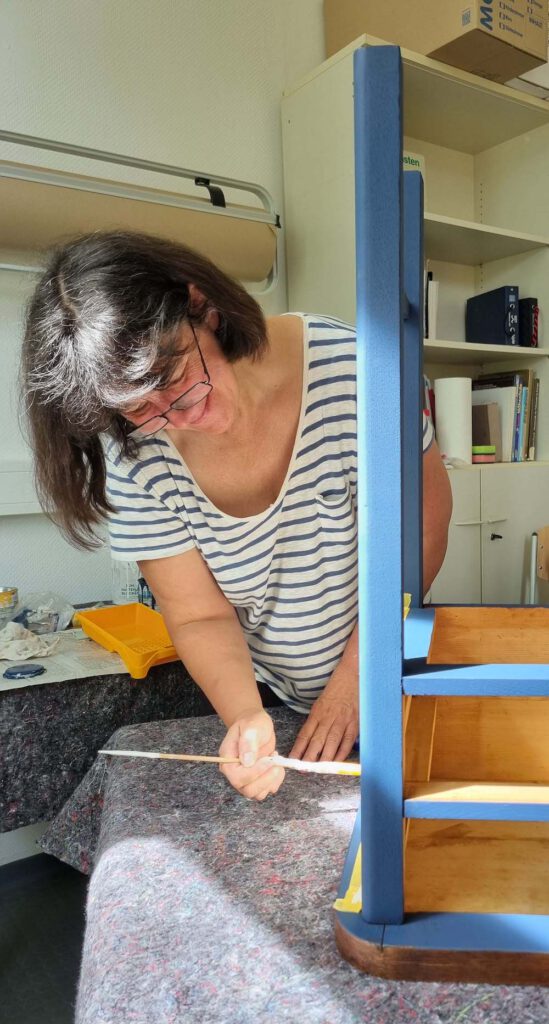 Frau bei der Arbeit in einer Werkstatt, die ein altes Möbelstück neu aufbereitet und blau anstreicht. Upcycling Möbel in Erfurt, Thüringen.