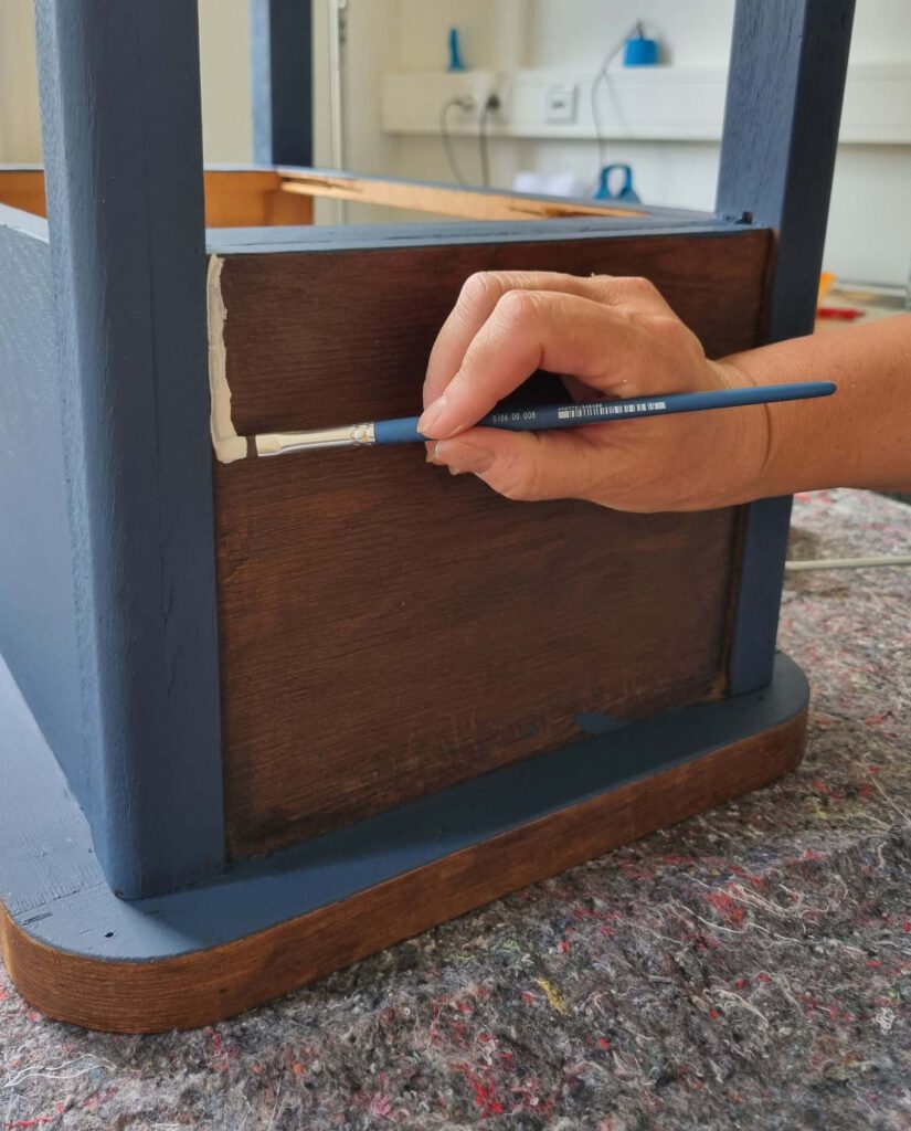 Nahaufnahme einer Hand von Ulrike Niewerth, Inhaberin von TREWIENS, die mit einem Pinsel ein restauriertes Möbelstück blau und weiß anstreicht. Upcycling von Möbeln in Thüringen